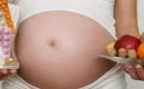 Pregnant woman holding a glass full of supplements and a plate of fruit