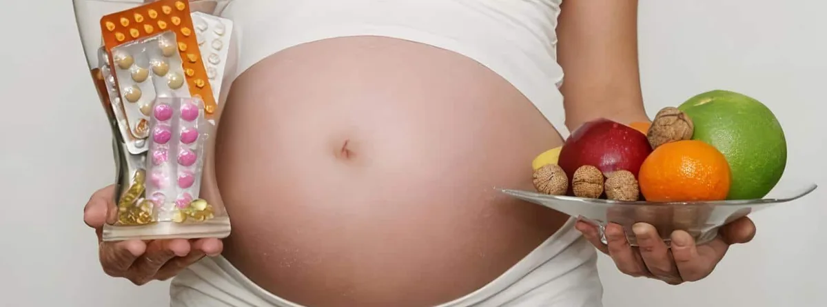 Pregnant woman holding a glass full of supplements and a plate of fruit
